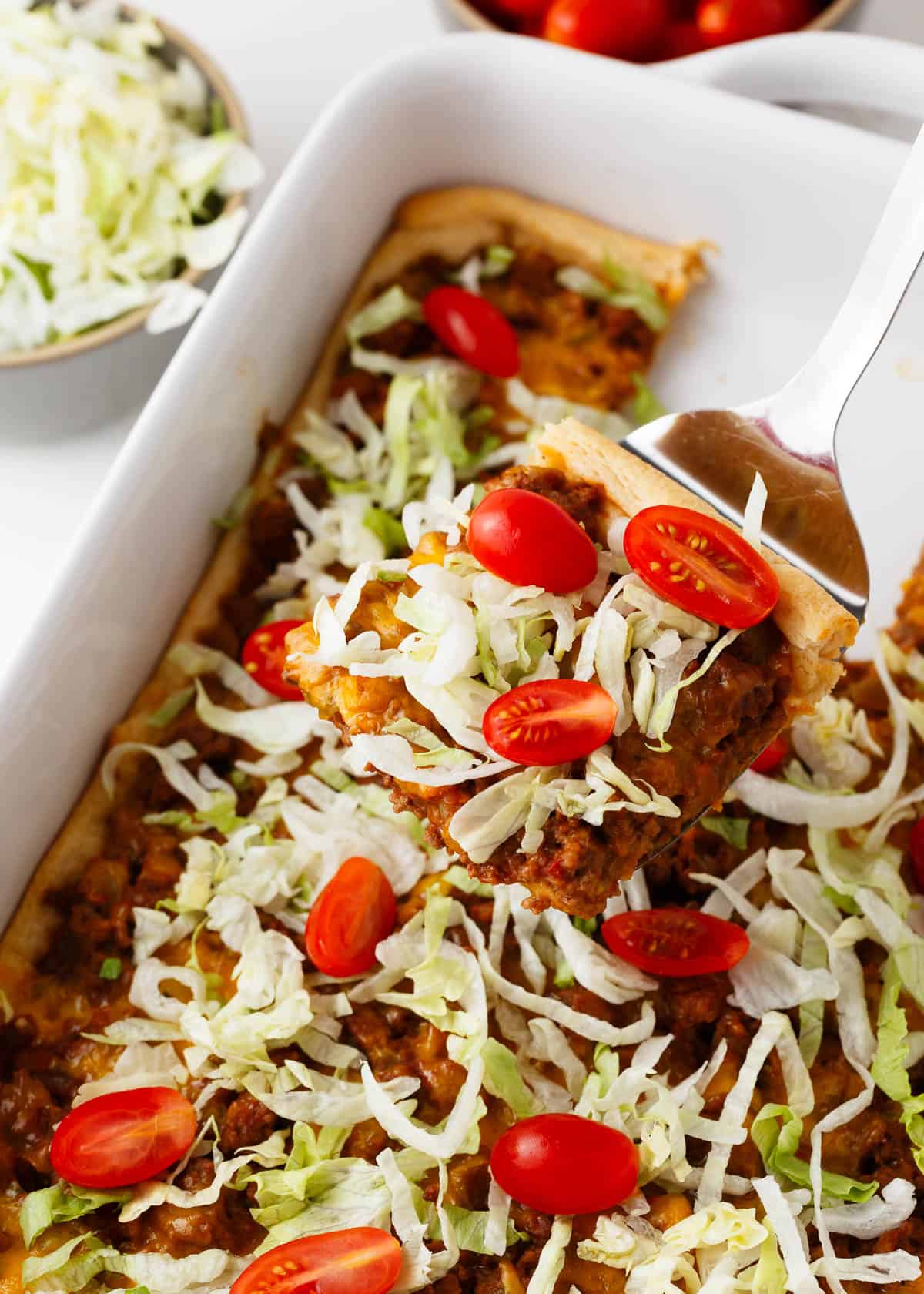 Crescent roll taco bake in a white baking dish with a server spatula.