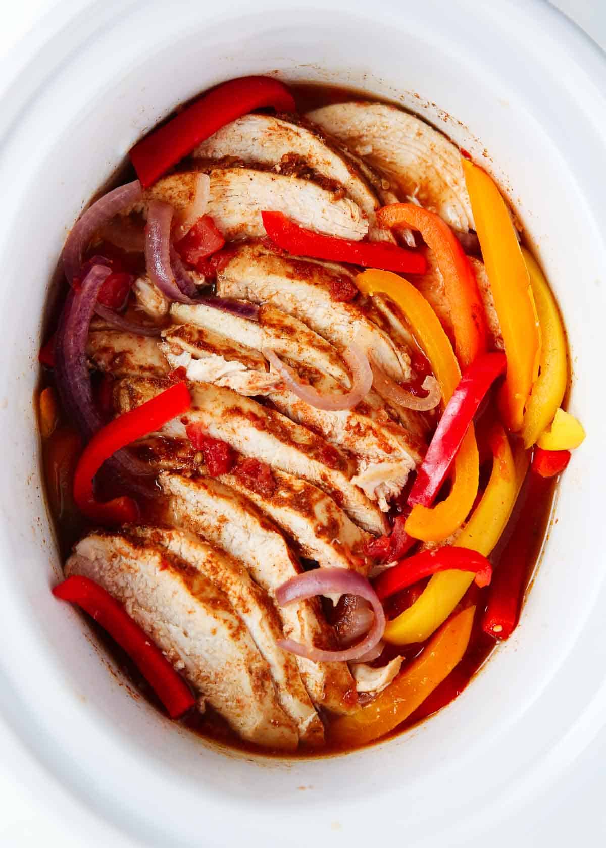 This dump-and-set recipe is an effortless way of making a flavorful Mexican-style dinner any night of the week. Easy crockpot chicken fajitas are made with juicy chicken, taco seasoning, and tender crispy veggies cooked low and slow until the flavors marry and it's ready to serve! Crockpot chicken fajitas in a white pot.
