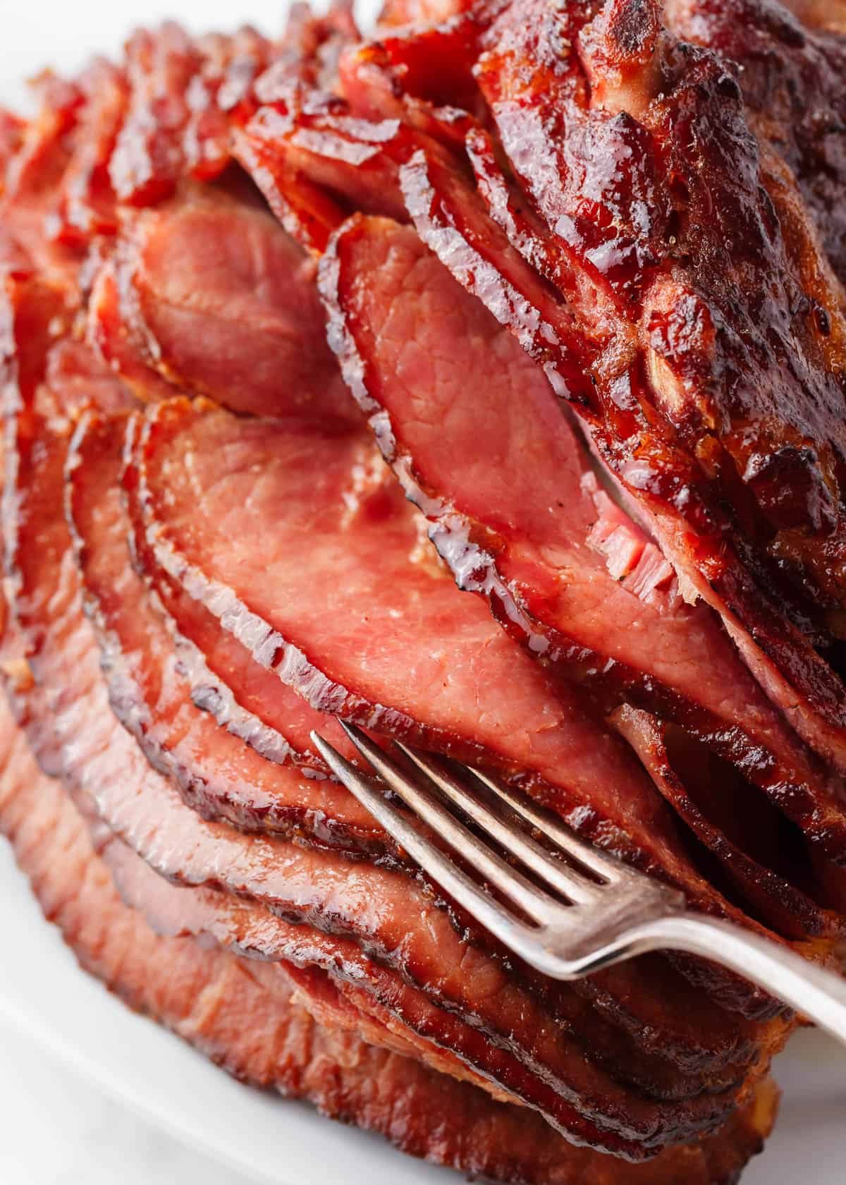 Honey baked ham recipe sliced with a fork between slices.