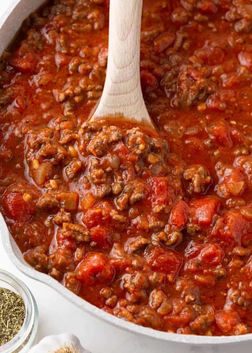 Meat sauce cooking in a skillet with wooden spoon.
