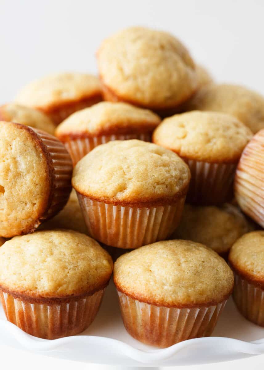 Stacked mini banana muffins on white cake plate. 