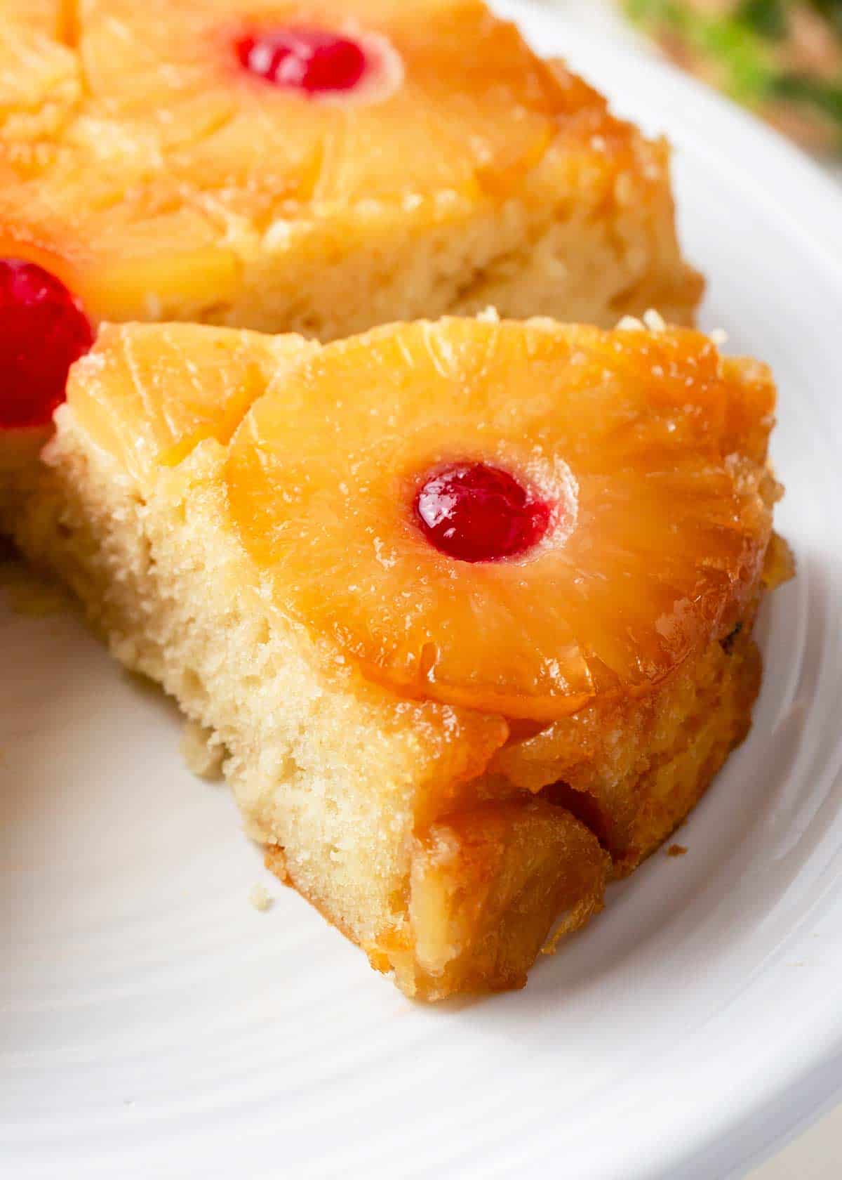 For a classic dessert that’s as impressive as it is delicious, try this easy pineapple upside down cake! Caramelized pineapple slices and bright cherries top this soft and moist vanilla buttermilk cake that's the perfect dessert for any occasion! Slice of Pineapple upside down cake on white platter.