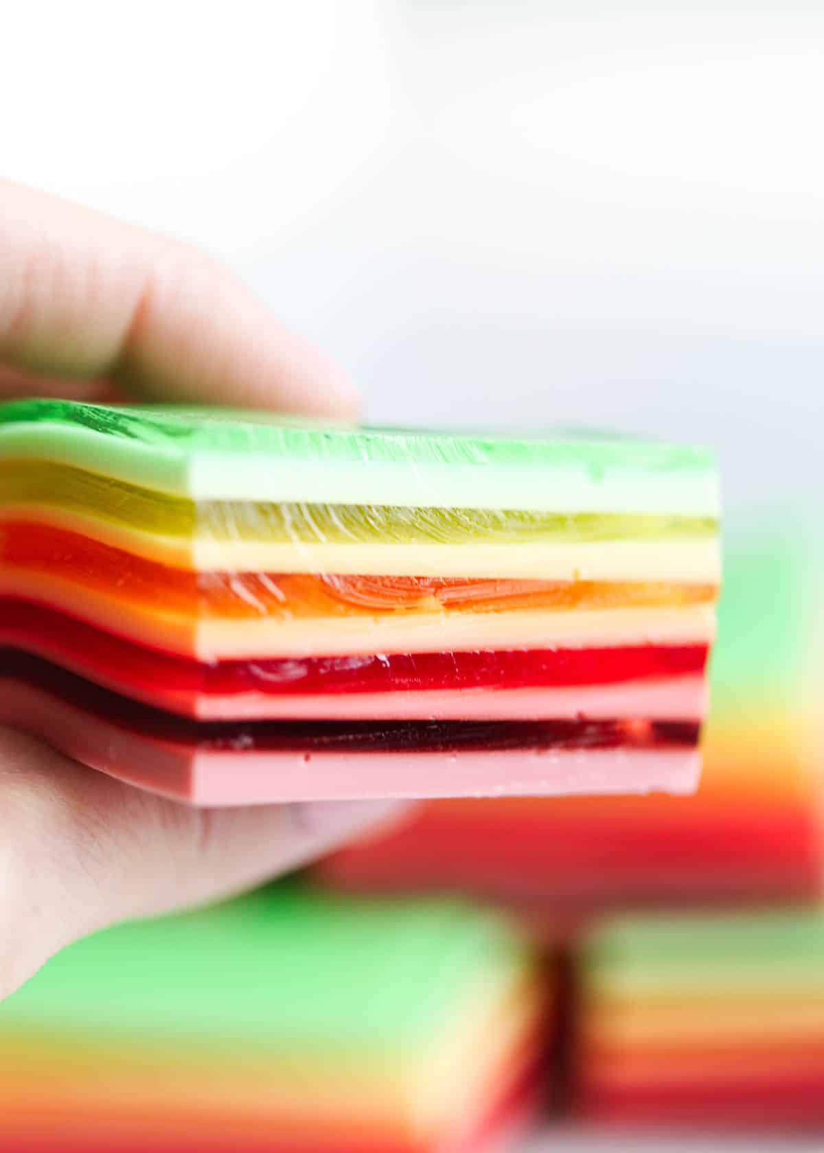 Rainbow jello being held up by a hand. 
