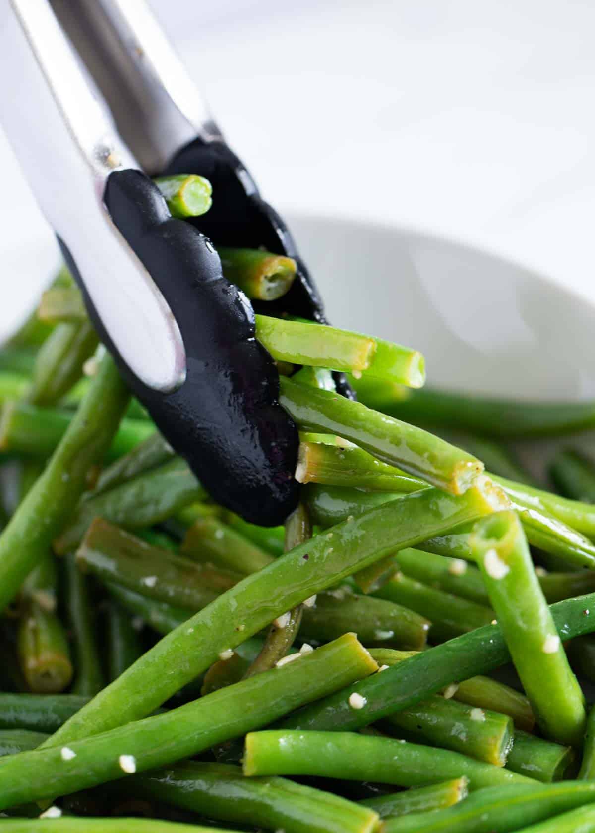 Tongs taking green beans out of bowl.
