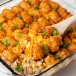 Tater tot casserole in a glass dish with a spoon.