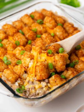 Tater tot casserole with cream of mushroom soup in a glass dish with a serving spoon.