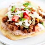 Tostada with toppings on a white plate.