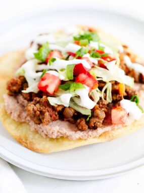 Tostada with toppings on a white plate.