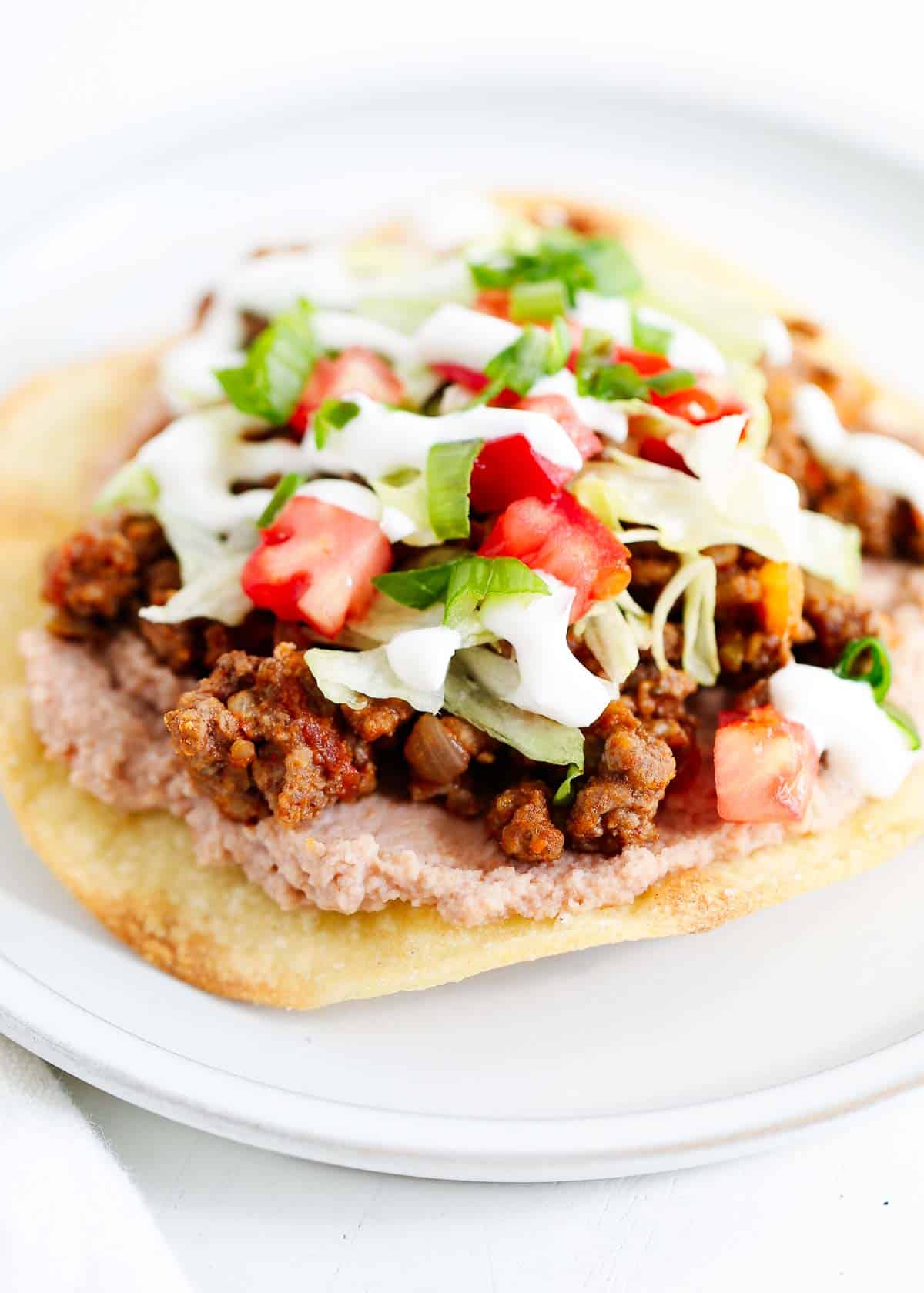 Tostada with toppings on a white plate.