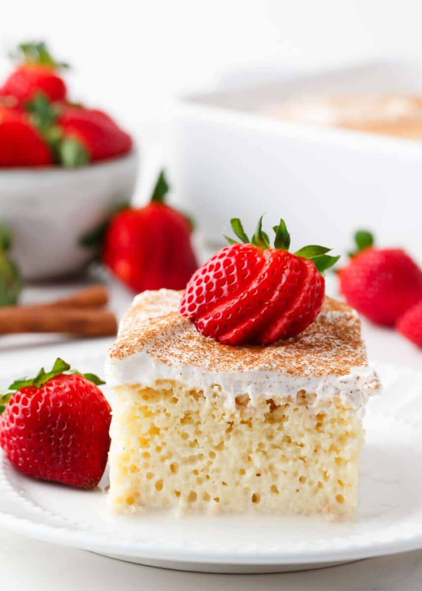 Slice of tres leches with strawberries on a plate.