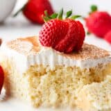 Slice of tres leches cake with strawberries on a white plate.