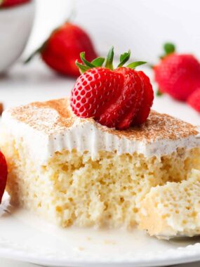 Slice of tres leches cake with strawberries on a white plate.