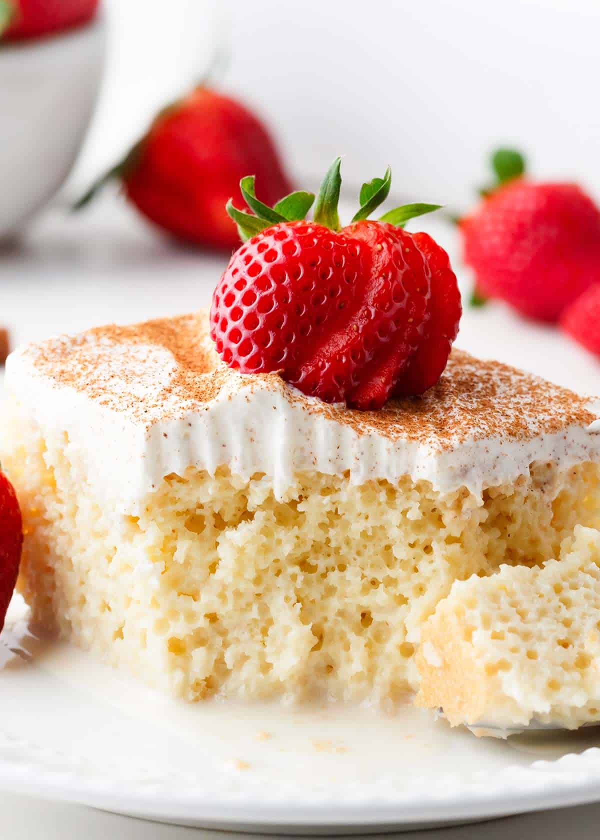 Slice of tres leches cake with strawberries on a white plate.