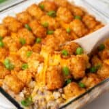 Tater tot casserole in a glass dish with a spoon.