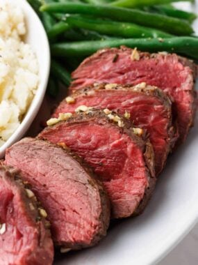 Sliced beef tenderloin roast on a white plate.