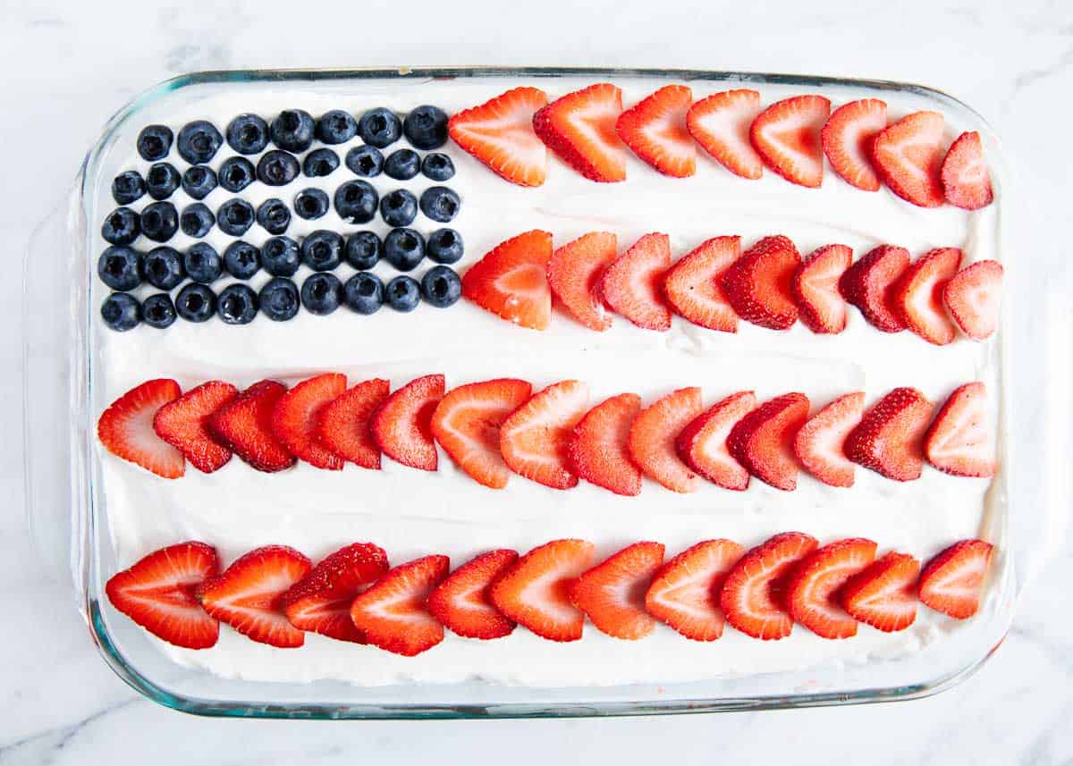 An overhead photo of a cake with a flag made out of strawberries and blueberries. 