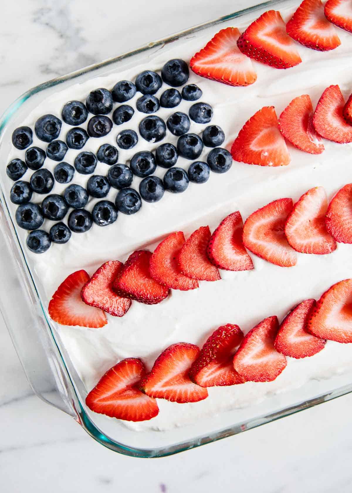 A jello poke cake with a flag made out of blueberries as the stars and strawberries as the stripes. 
