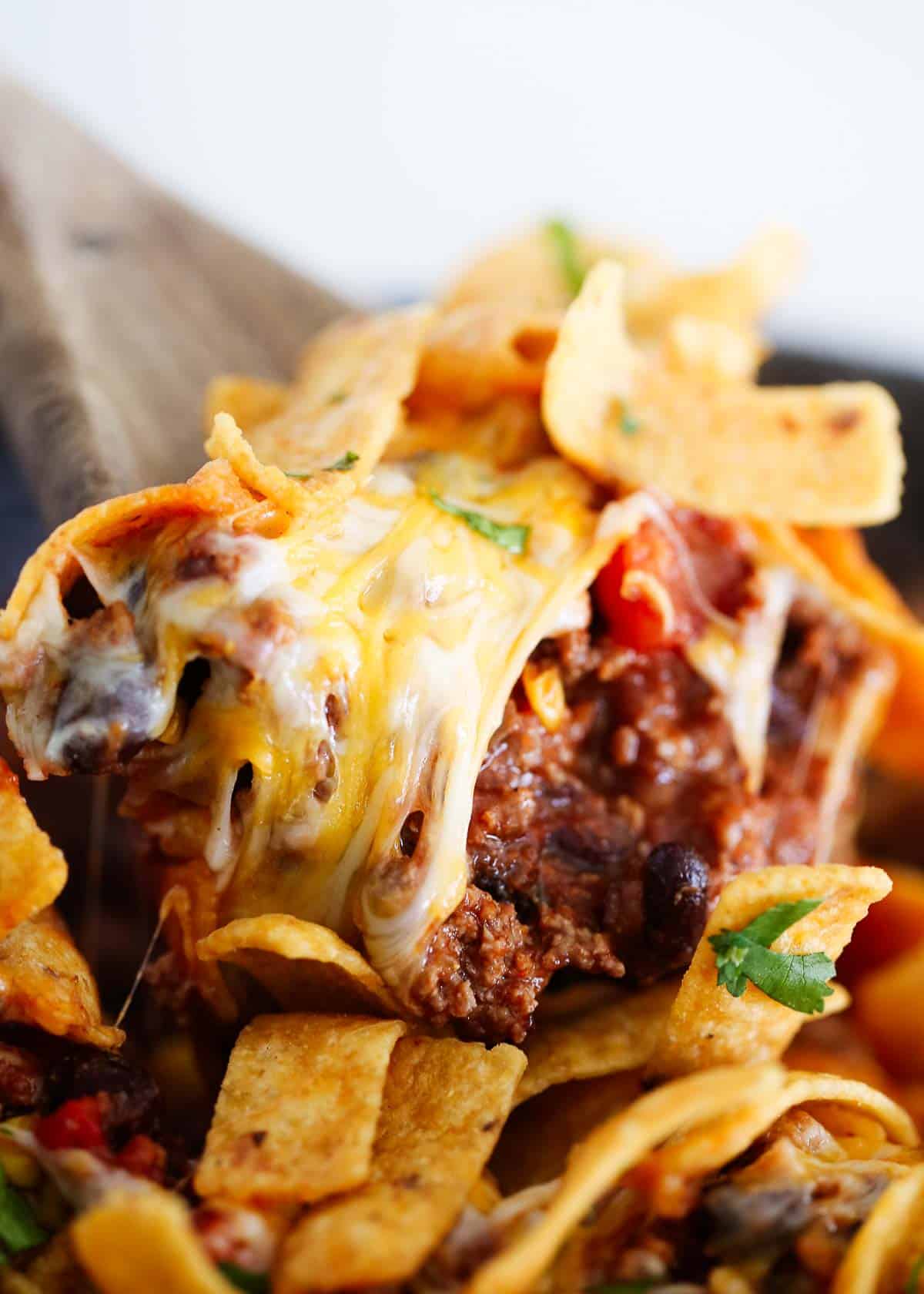 This Frito pie is made with a taco seasoned ground beef base with beans and corn then baked with plenty of cheese and crunchy Fritos. It's a family friendly meal everyone loves! Serving Frito pie with a serving spoon.