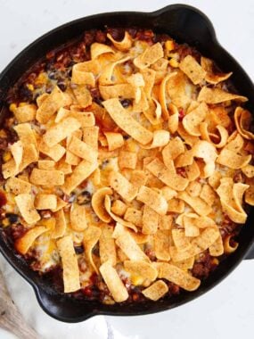 Easy Frito pie in a cast iron skillet topped with melted cheese, crunchy Fritos, and fresh cilantro.