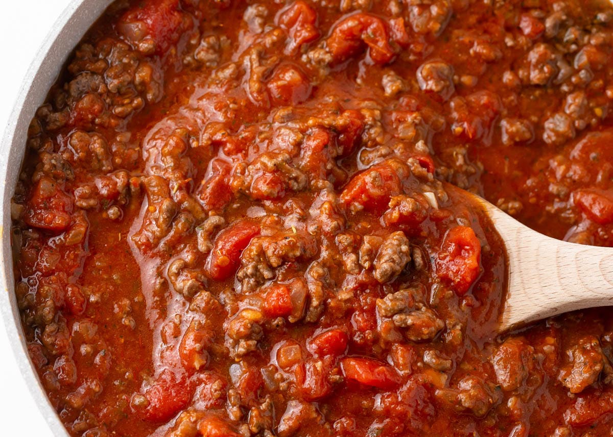 Spaghetti meat sauce simmering in a skillet with a wooden spoon.