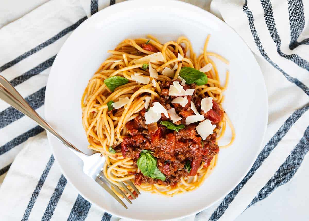 Spaghetti bolognese on a plate with striped linens under it.