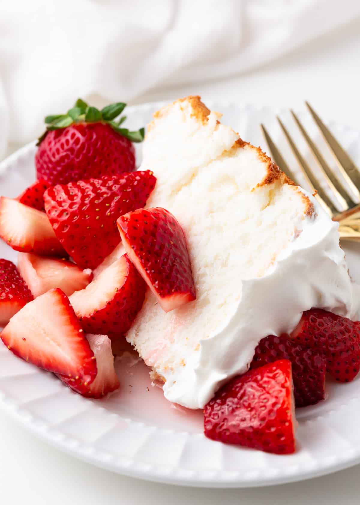 Slice of angel food cake with whipped cream and strawberries. 