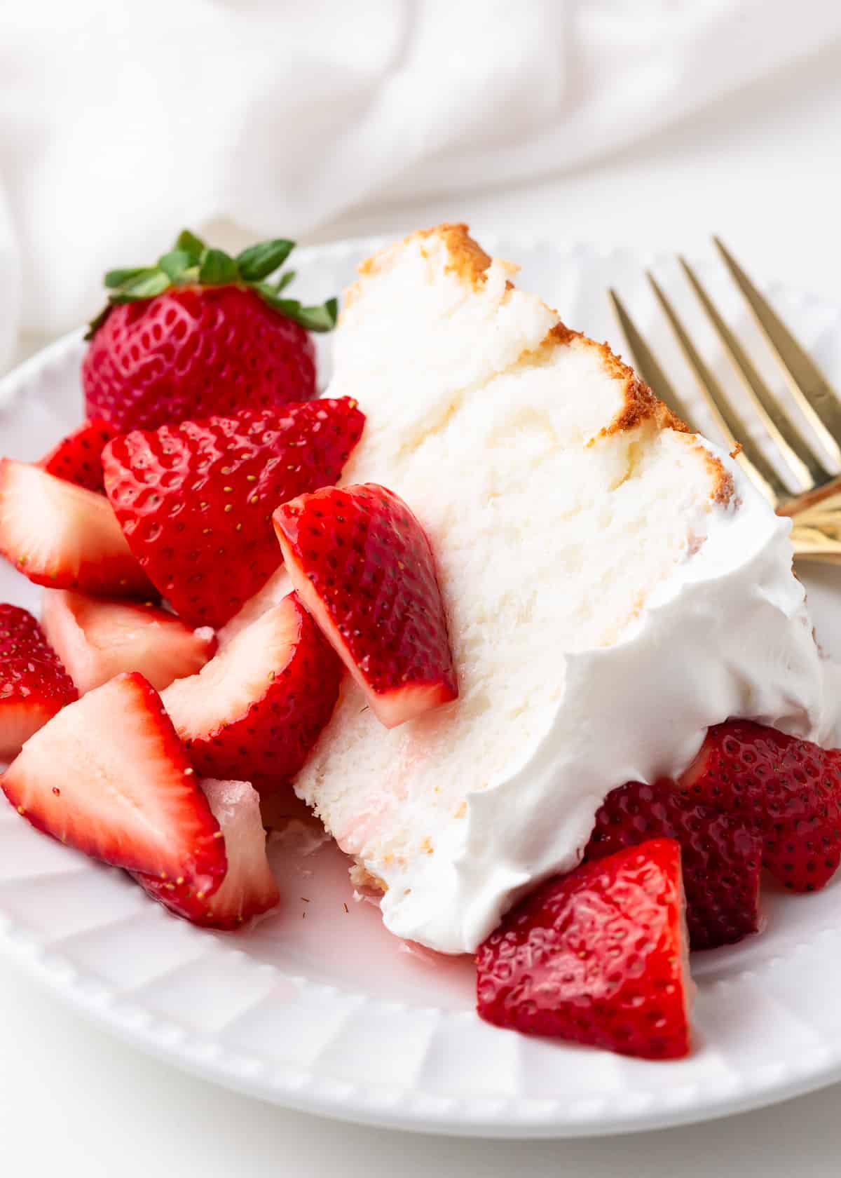 Slice of angel food cake with whipped cream and strawberries.