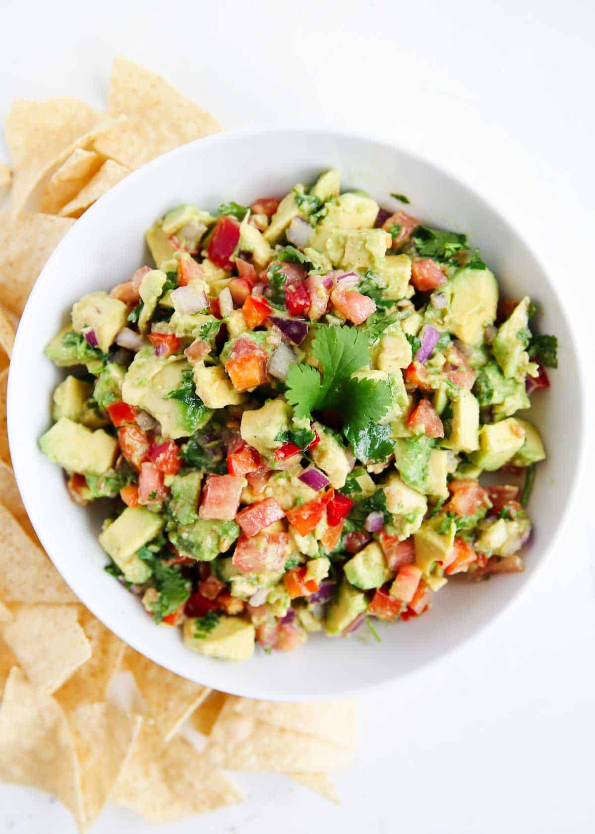 A white bowl with avocado salsa and chips on the side for scooping.
