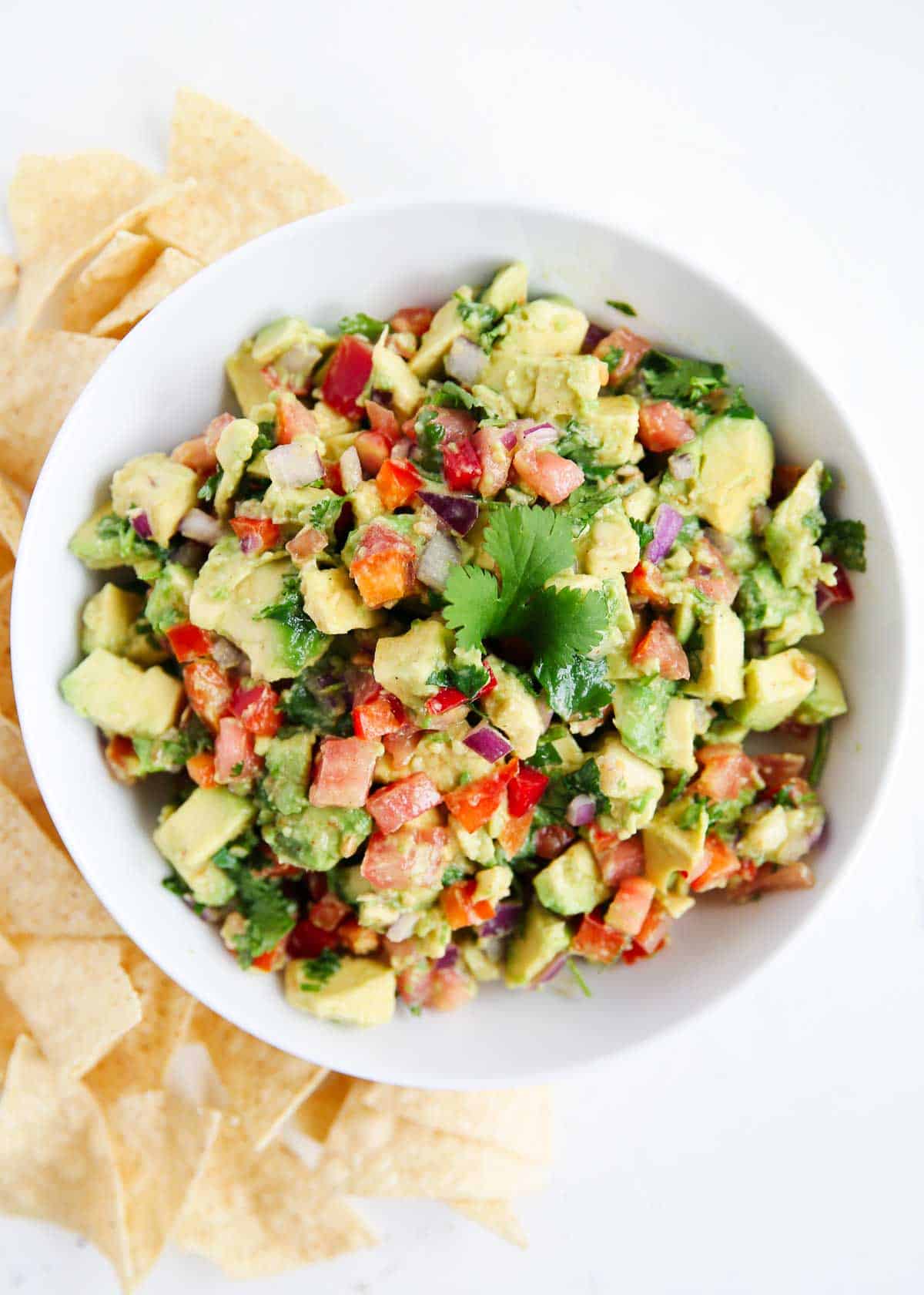 This avocado salsa is the best summer appetizer! It's fresh and flavorful with chunks of avocado, tomatoes, red onions, bell peppers, and cilantro then tossed with vibrant lime. A white bowl with avocado salsa and chips on the side for scooping.