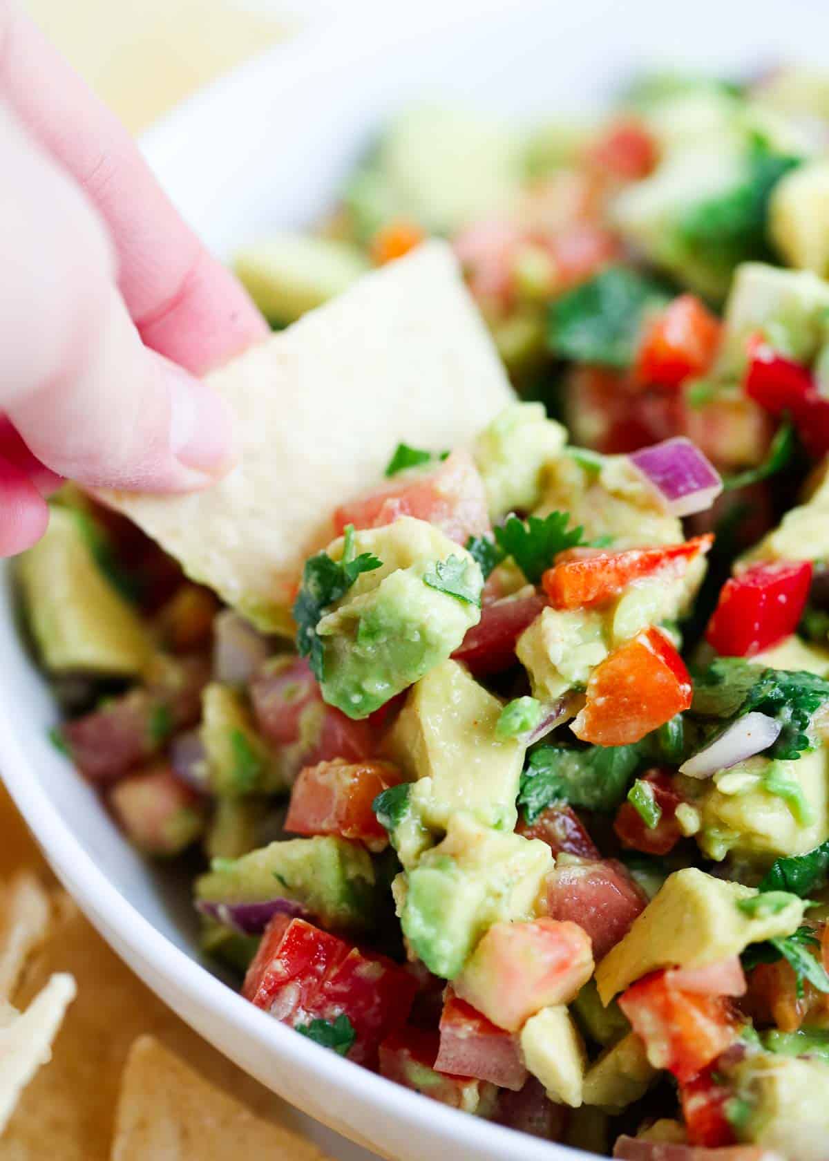 A tortilla chip being dipped into a bowl of avocado salsa.
