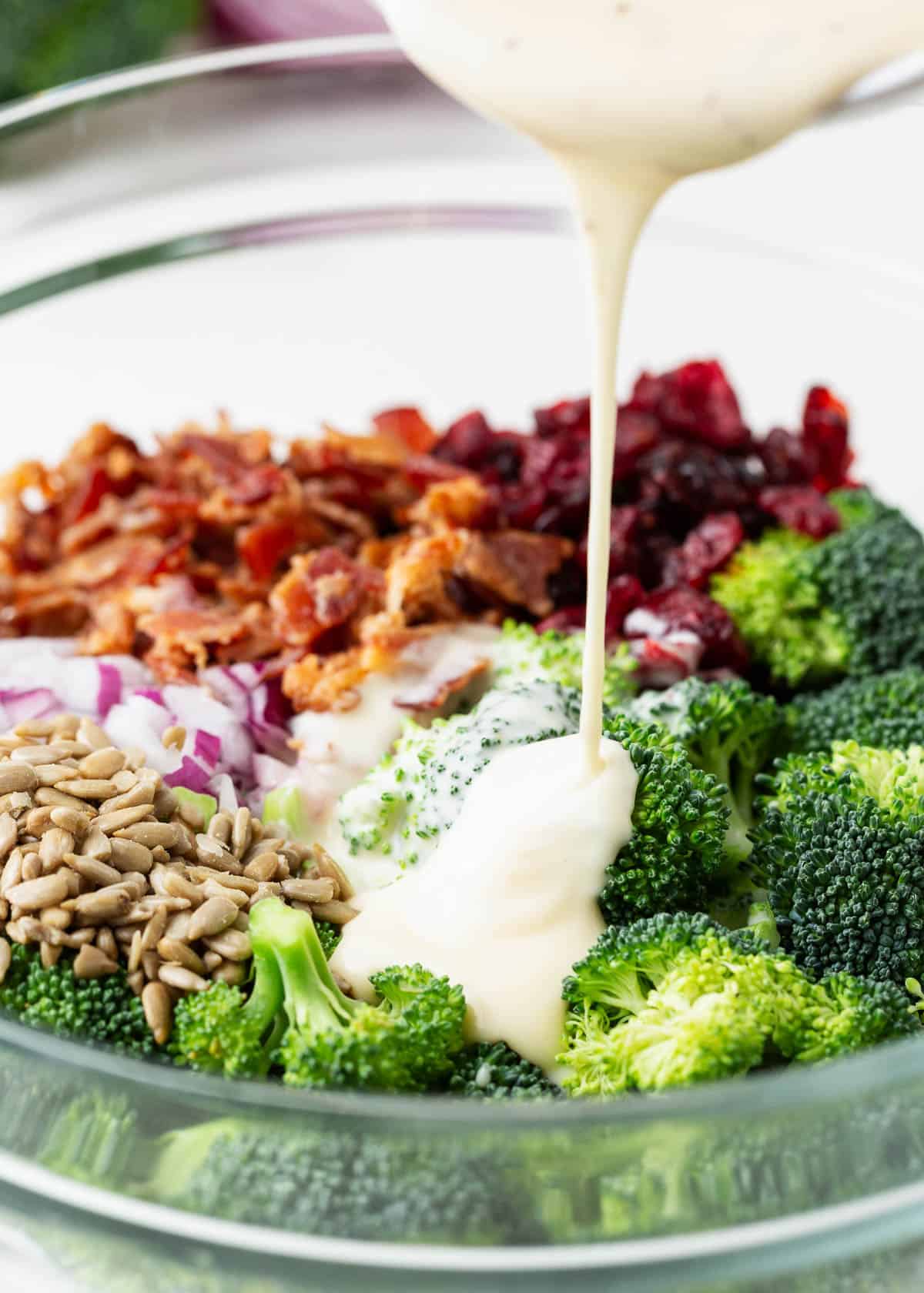 Pouring dressing over broccoli salad with bacon.