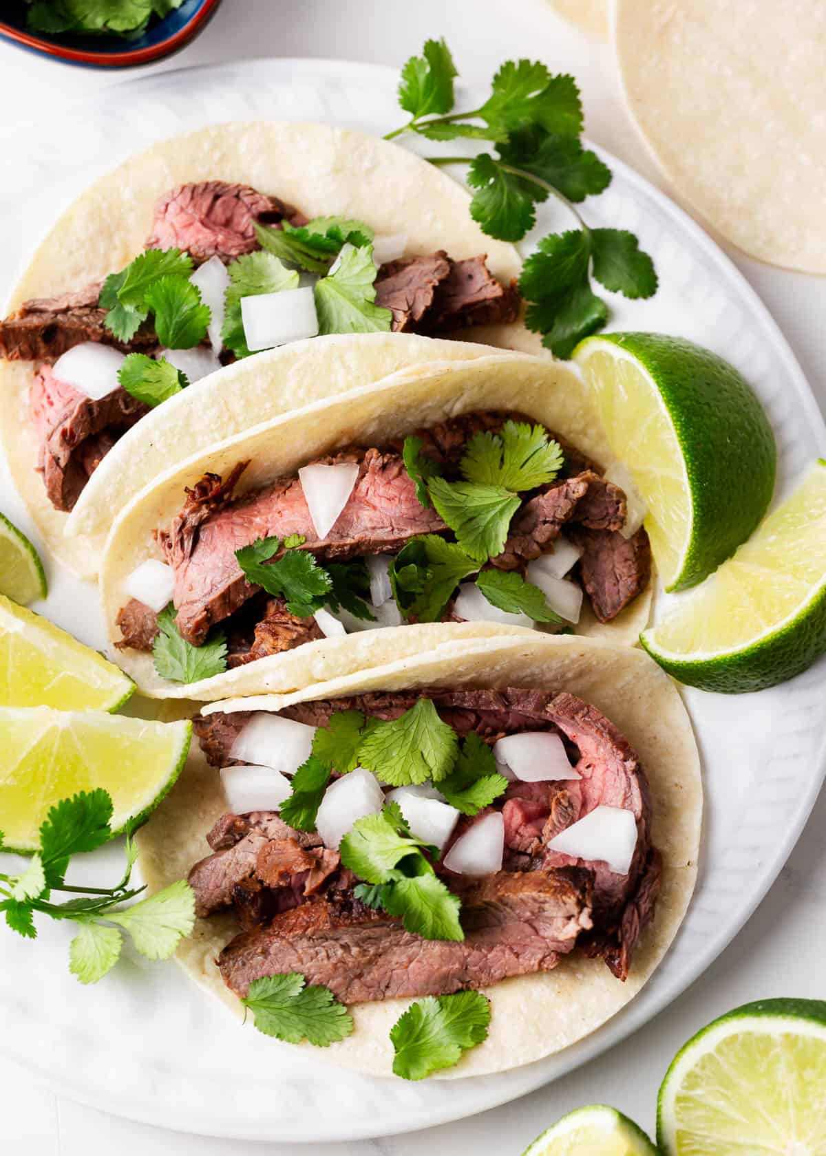 Three carne asada tacos on a plate.