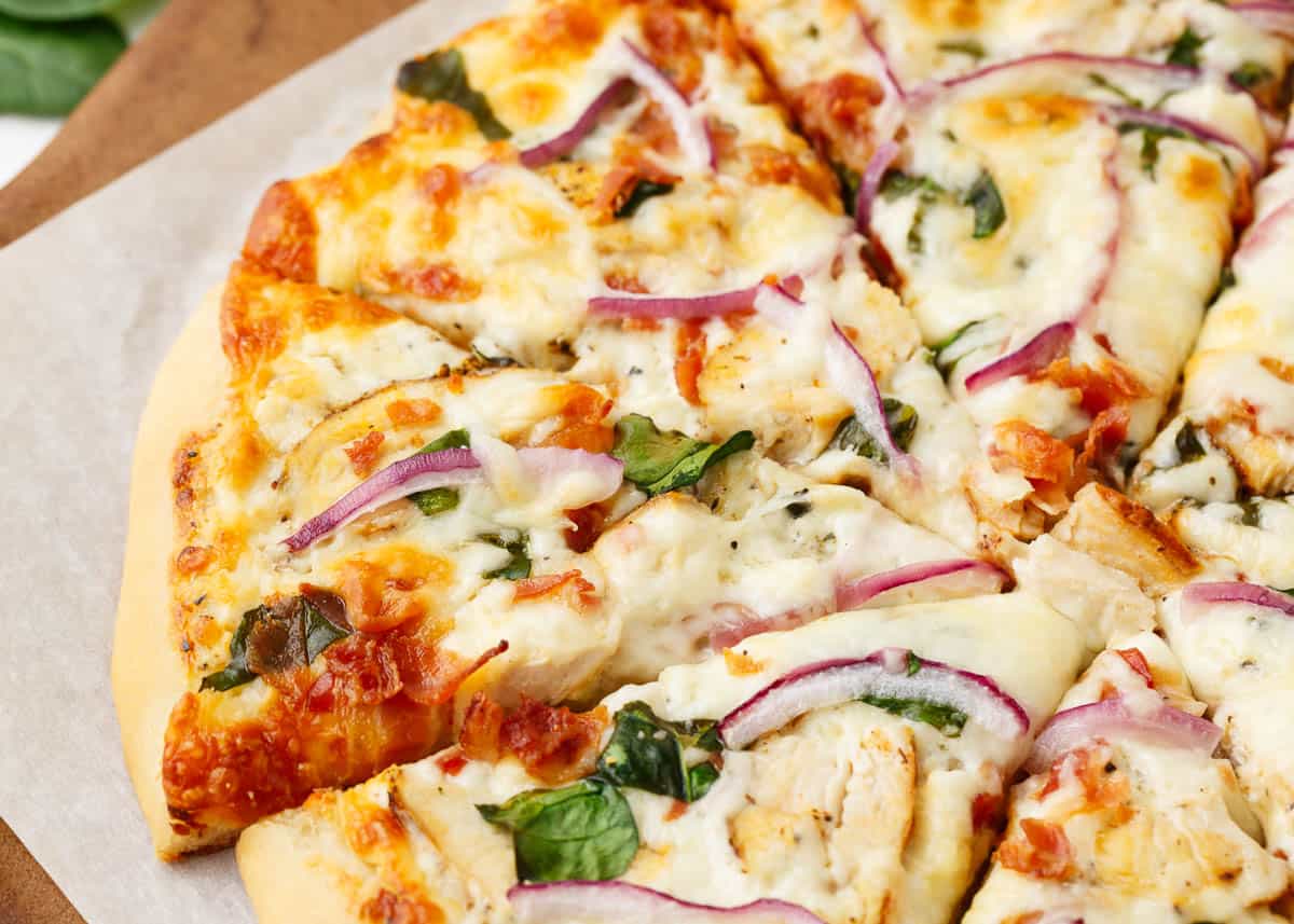 Sliced chicken alfredo pizza on baking stone.