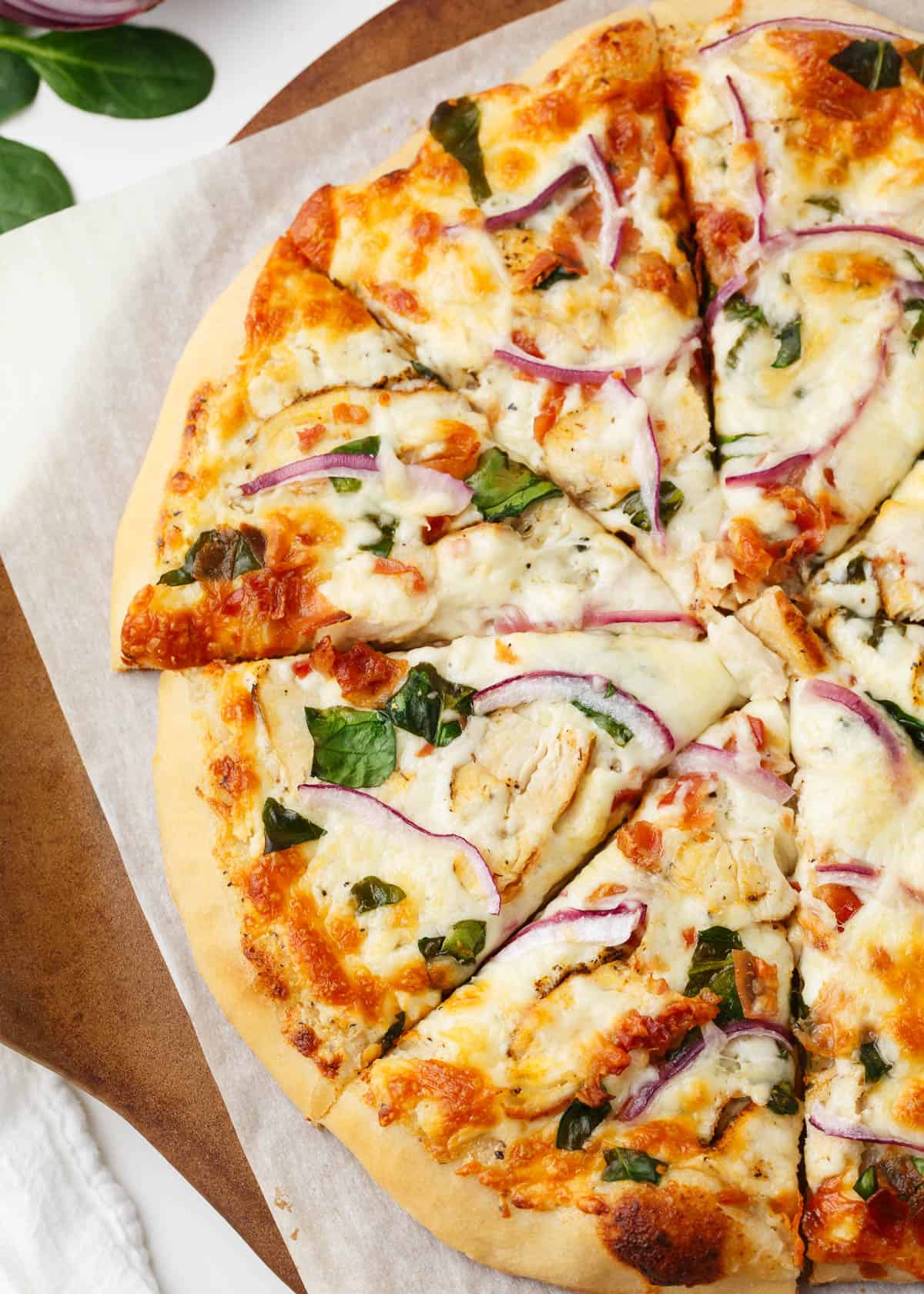 Sliced chicken alfredo pizza on parchment paper placed on pizza stone.