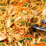 Chicken chow mein in a large skillet with serving tongs.