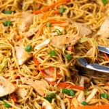 Chicken chow mein in a large skillet with serving tongs.