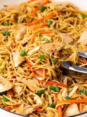 Chicken chow mein in a large skillet with serving tongs.