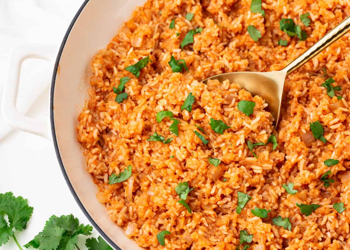 Mexican rice in a white skillet with garnish and gold serving spoon.