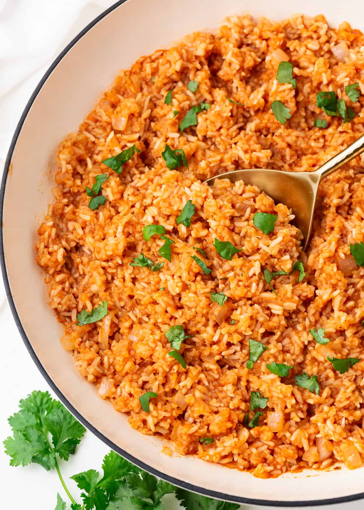 White skillet filled with Mexican rice, topped with cilantro garnish and a serving spoon.