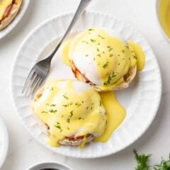 Eggs Benedict made at home with poached eggs and a hollandaise sauce served on a white plate.