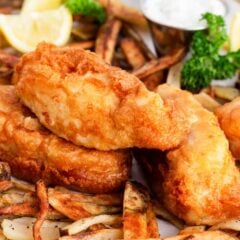 British fish and chips on a piece of parchment paper with lemon wedge and tartar sauce.