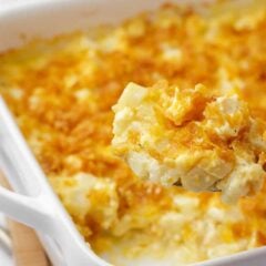 Serving spoon scooping funeral potatoes showing melted cheese and tender potatoes.