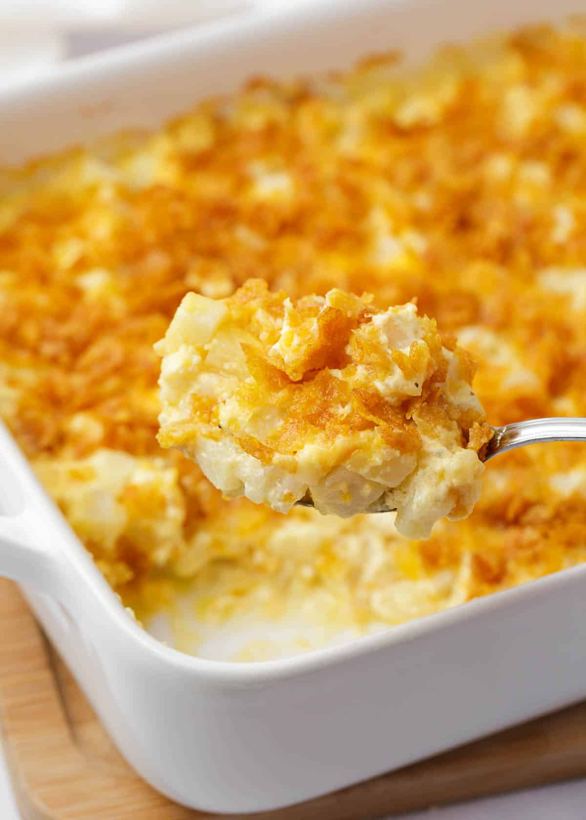 Spoonful of funeral potatoes in a white baking dish.
