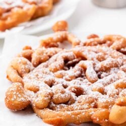 Funnel cake on a white plate with powdered sugar.