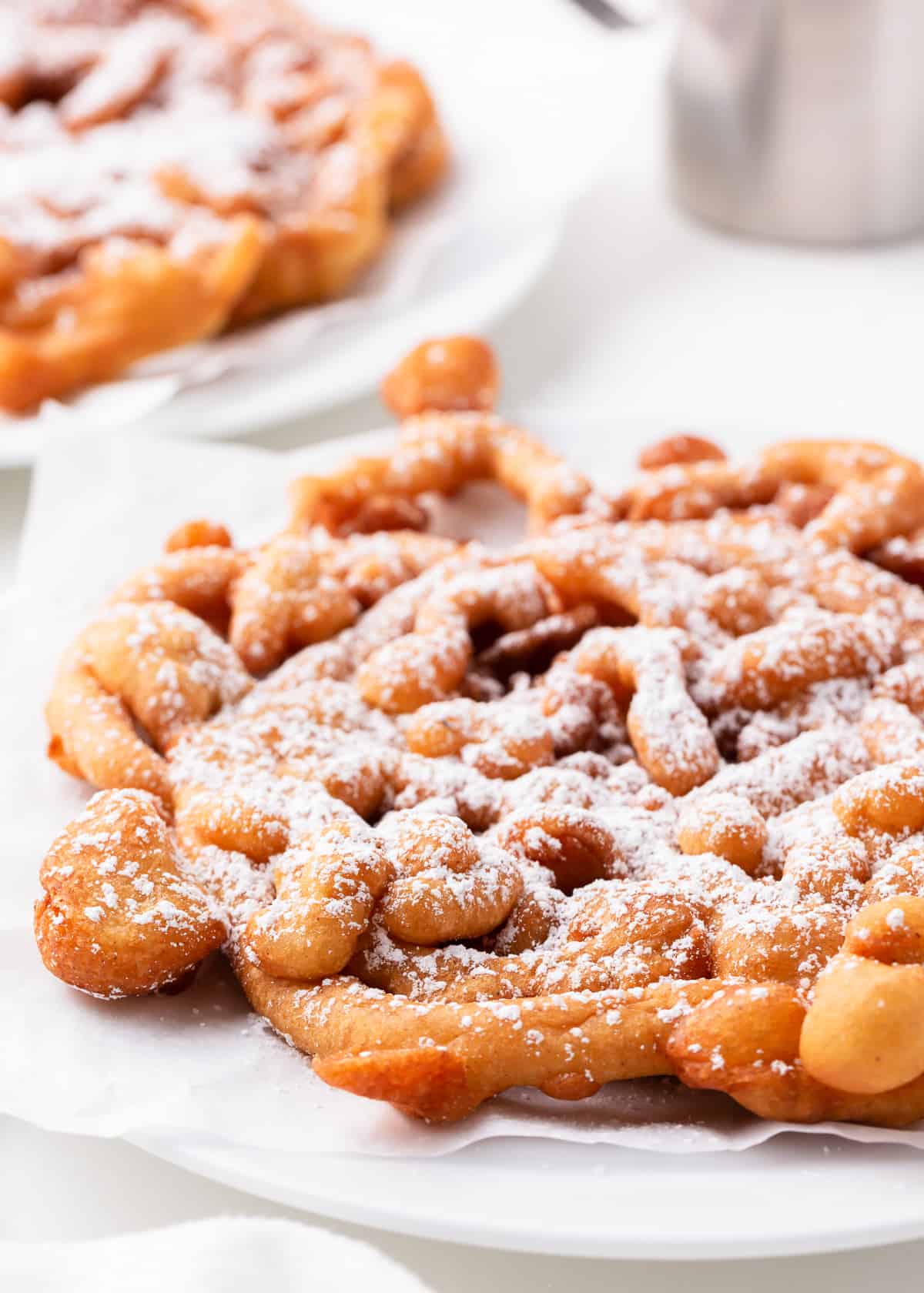 Funnel cake on a white plate with powdered sugar.