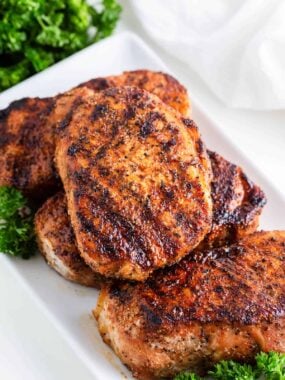 Grilled pork chops on a white plate with parsley.