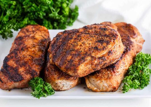 Grilled pork chops on a white platter with parsley.