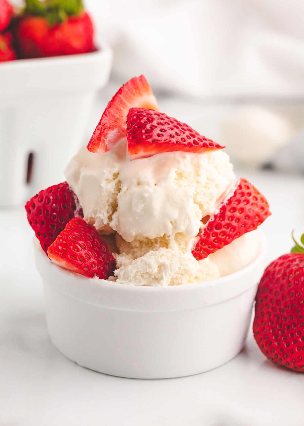 Vanilla homemade ice cream in a white bowl with sliced strawberries on top.