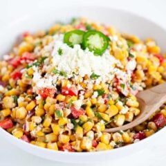 Mexican street corn salad in a white bowl with a wooden serving spoon.
