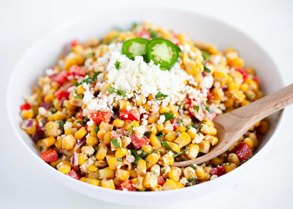 Mexican street corn salad in a white bowl with a wooden serving spoon.